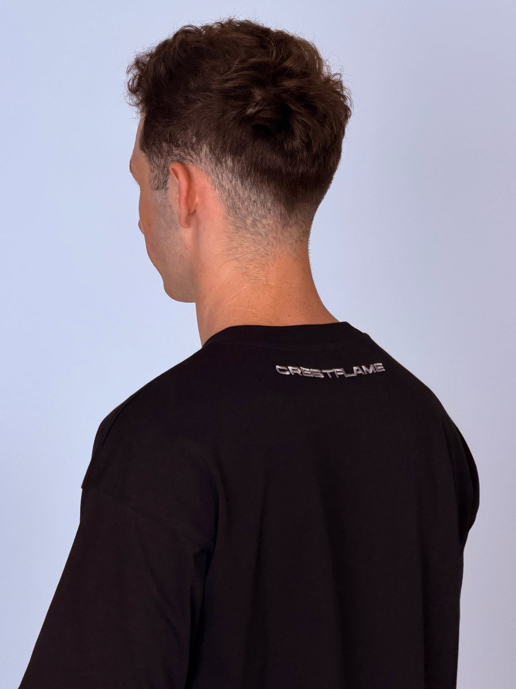 Person wearing a black long-sleeve shirt with a brand logo on the back against a light gray background