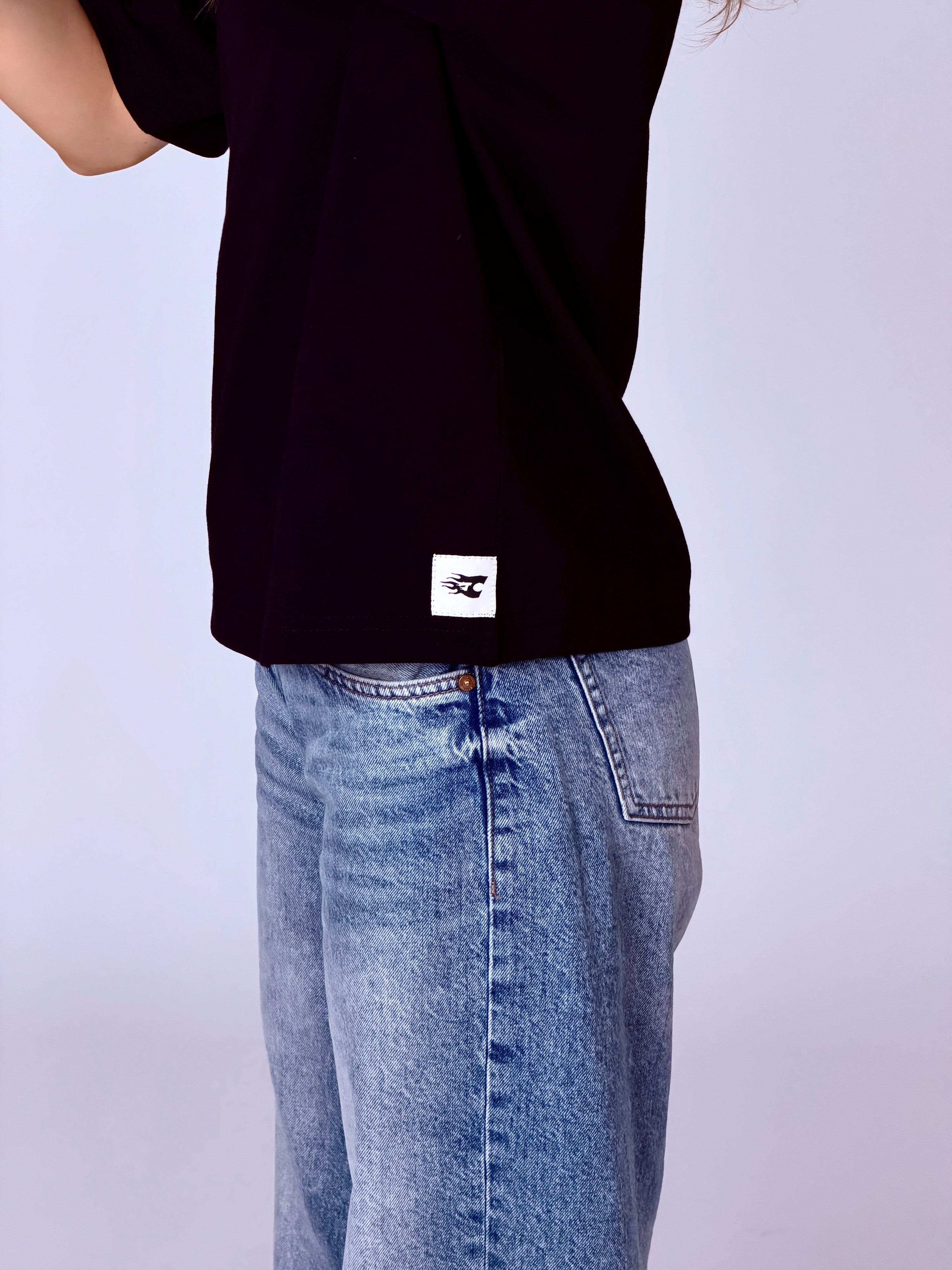Person wearing a black t-shirt with a white logo and blue jeans on a light gray background