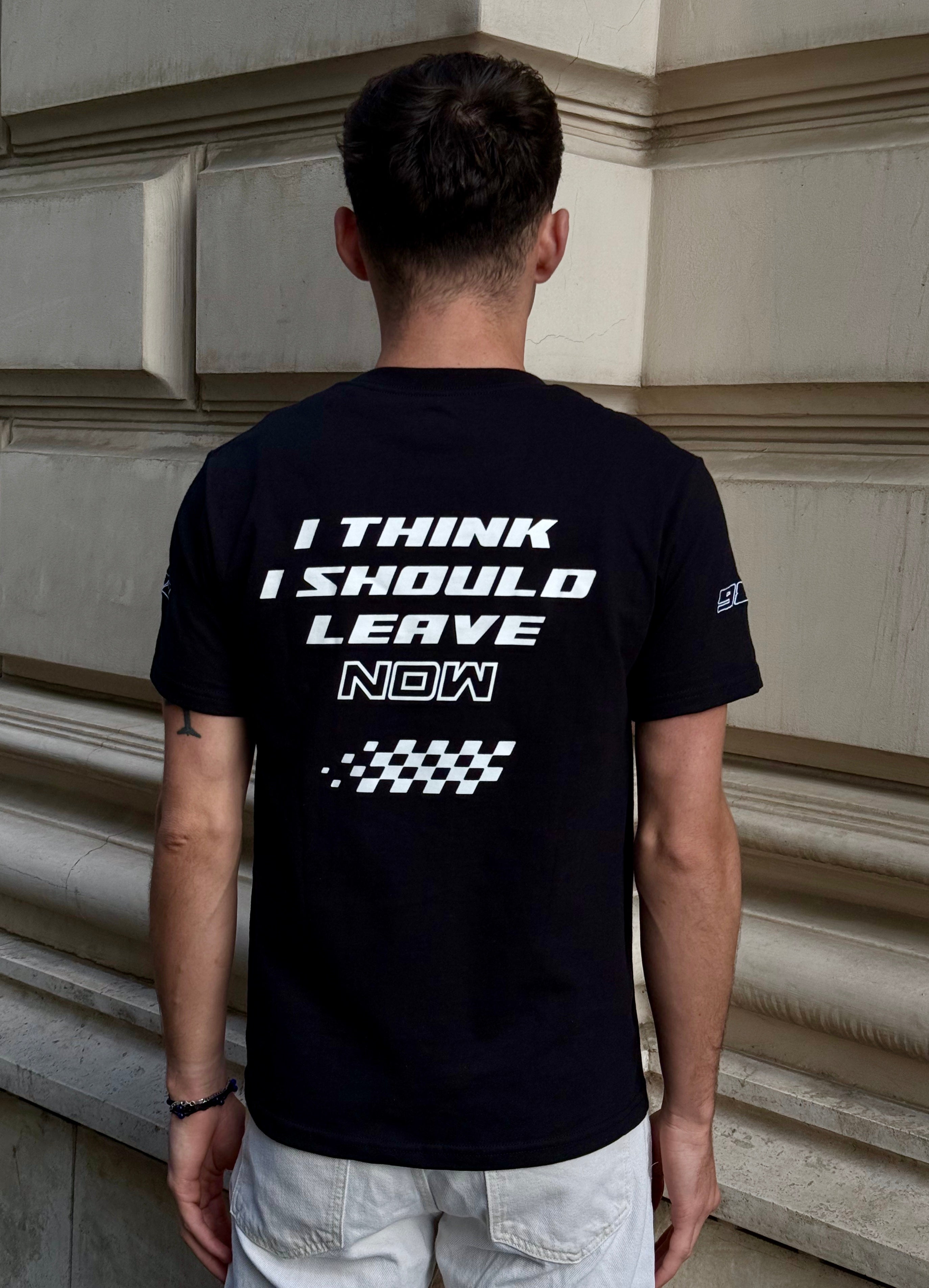 Person wearing a black t-shirt with text on the back, standing against a building wall.