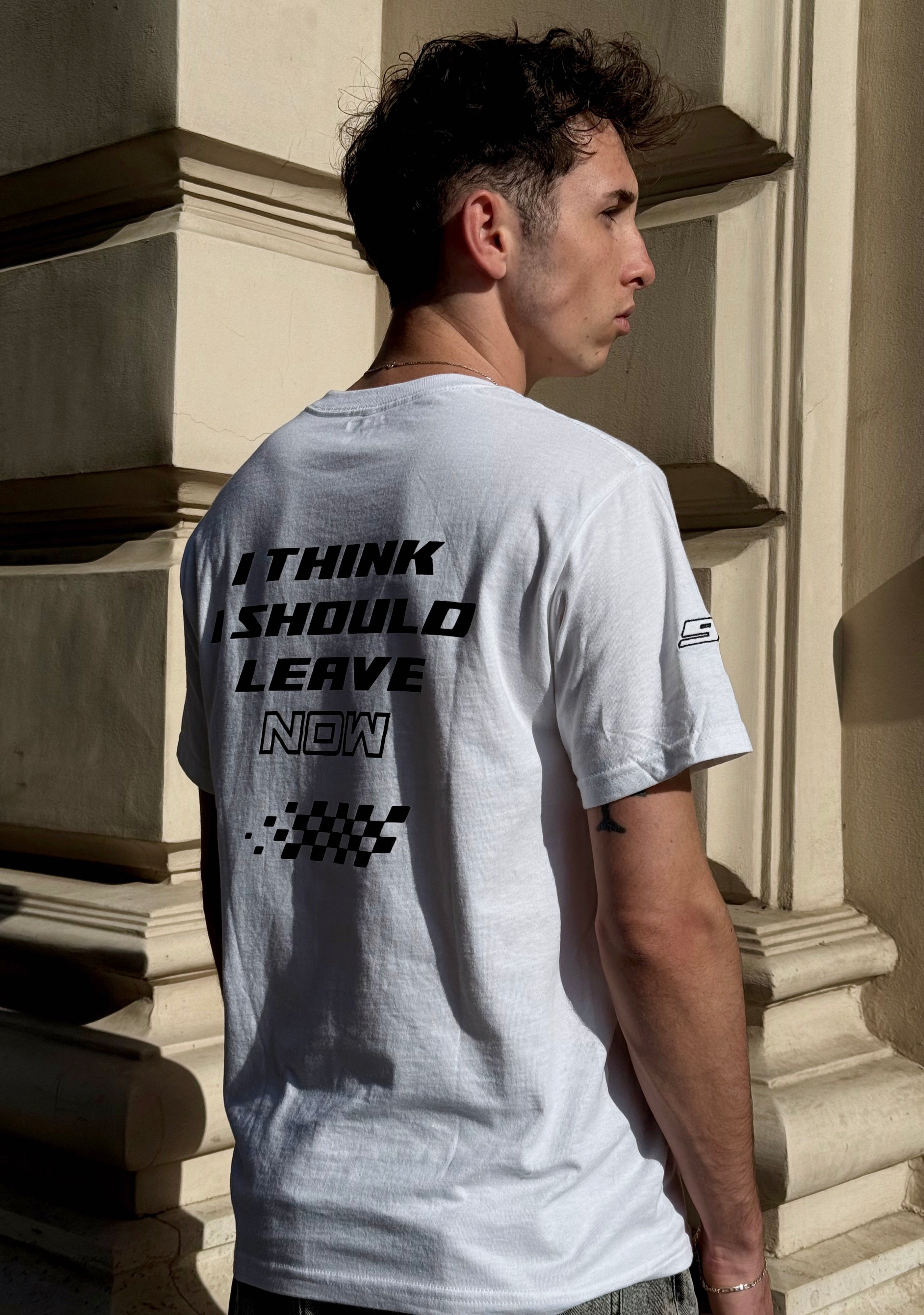 Man wearing a white t-shirt with text on the back, standing outdoors.