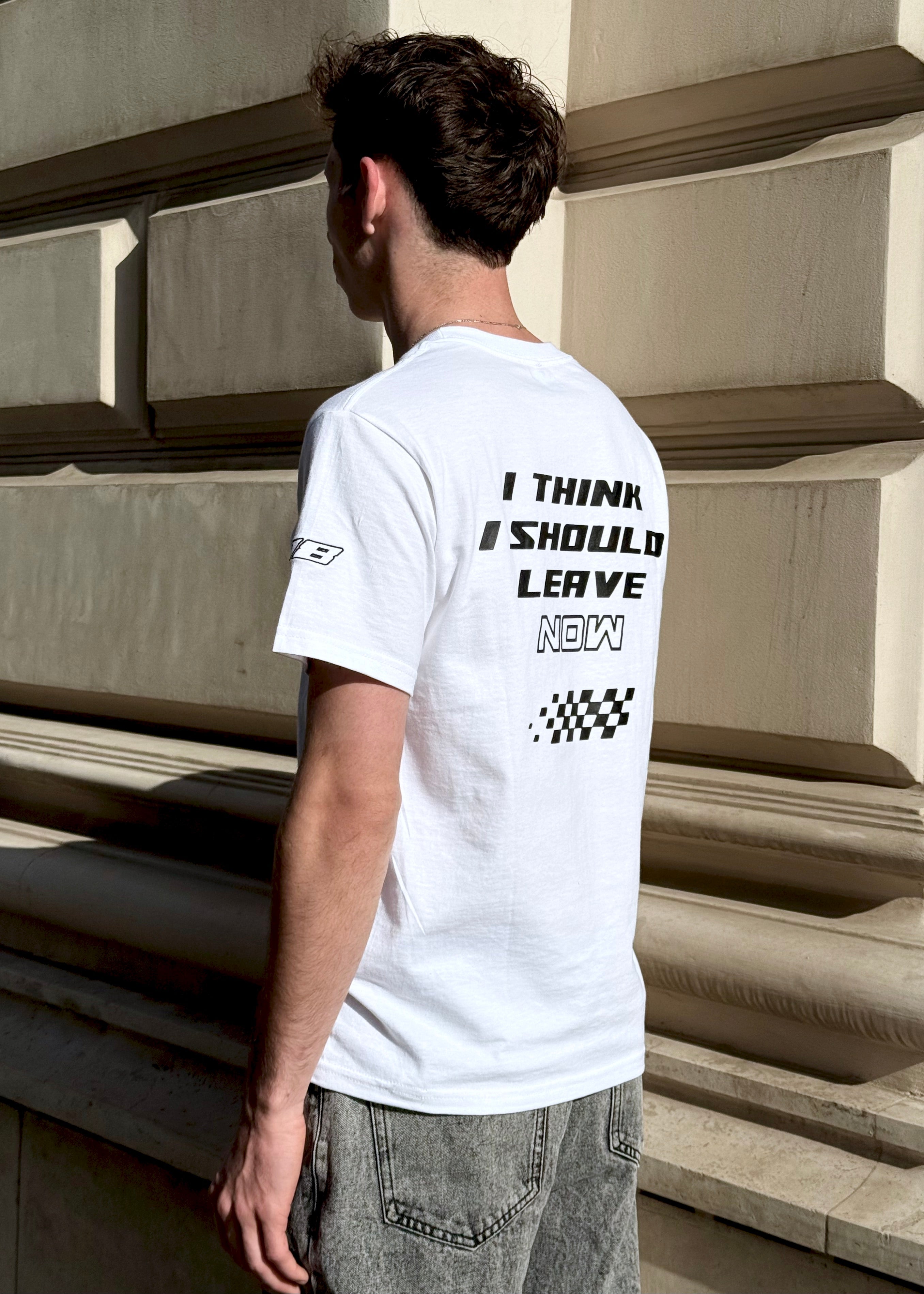 Person wearing a white t-shirt with text standing against a stone wall.