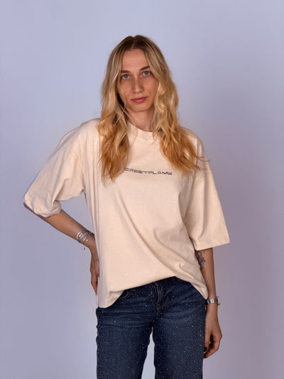 Person wearing a beige sweater and dark jeans against a light purple background