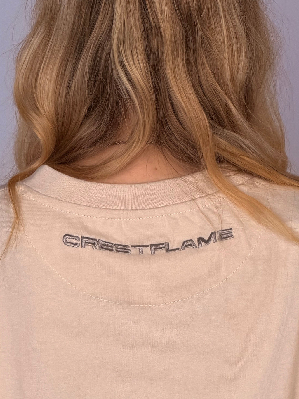 Beige shirt with 'GREATFLAME' logo on the back, worn by a person with blonde hair.