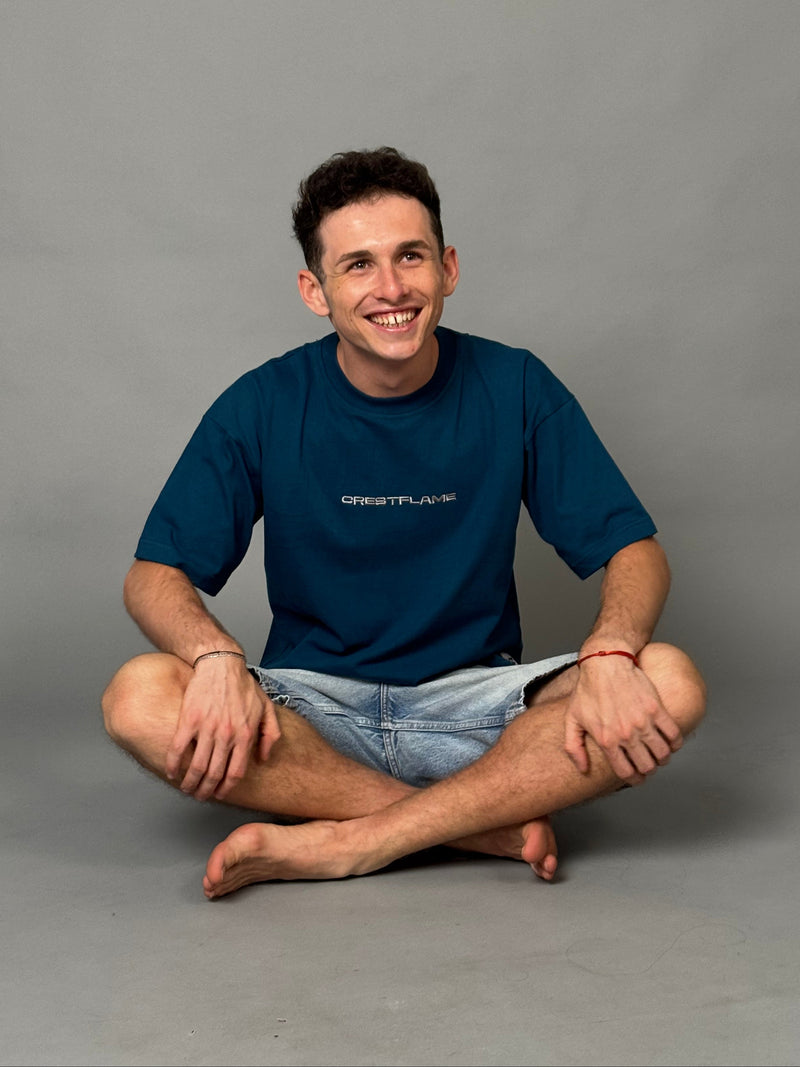 Man in a blue shirt and denim shorts sitting on a gray floor.