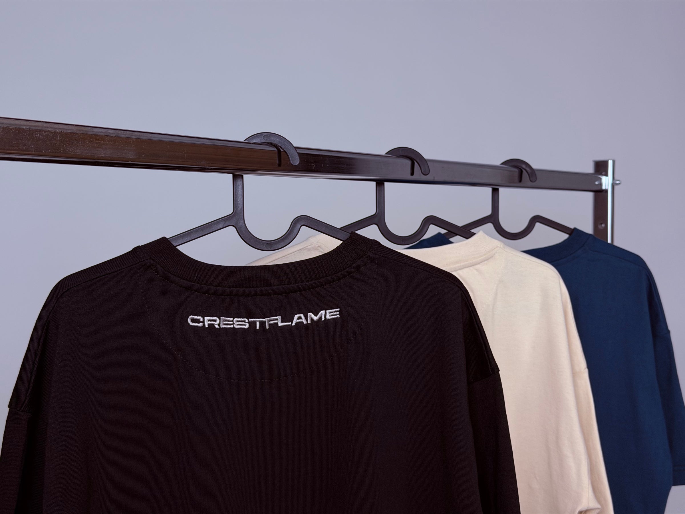 Black, beige, and blue sweatshirts hanging on a rack with 'CRESTFLAME' branding.