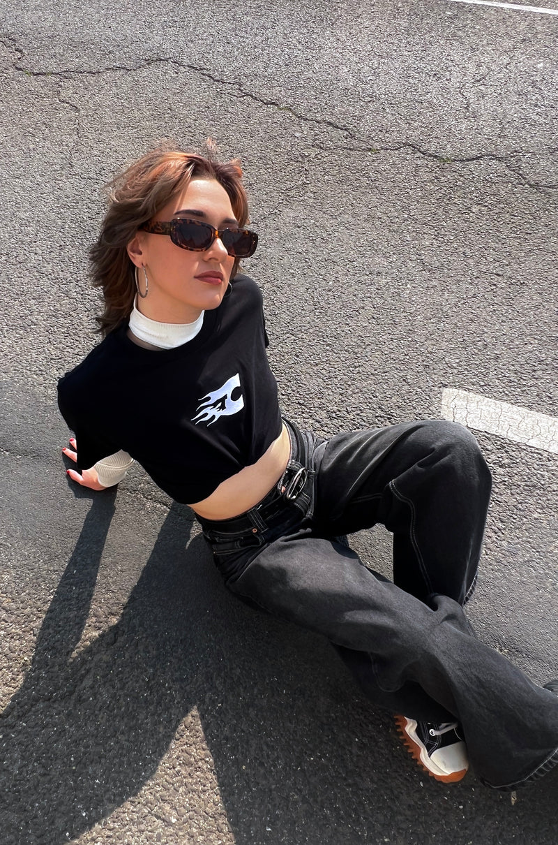 Person sitting on a cracked asphalt surface wearing sunglasses and black clothing.