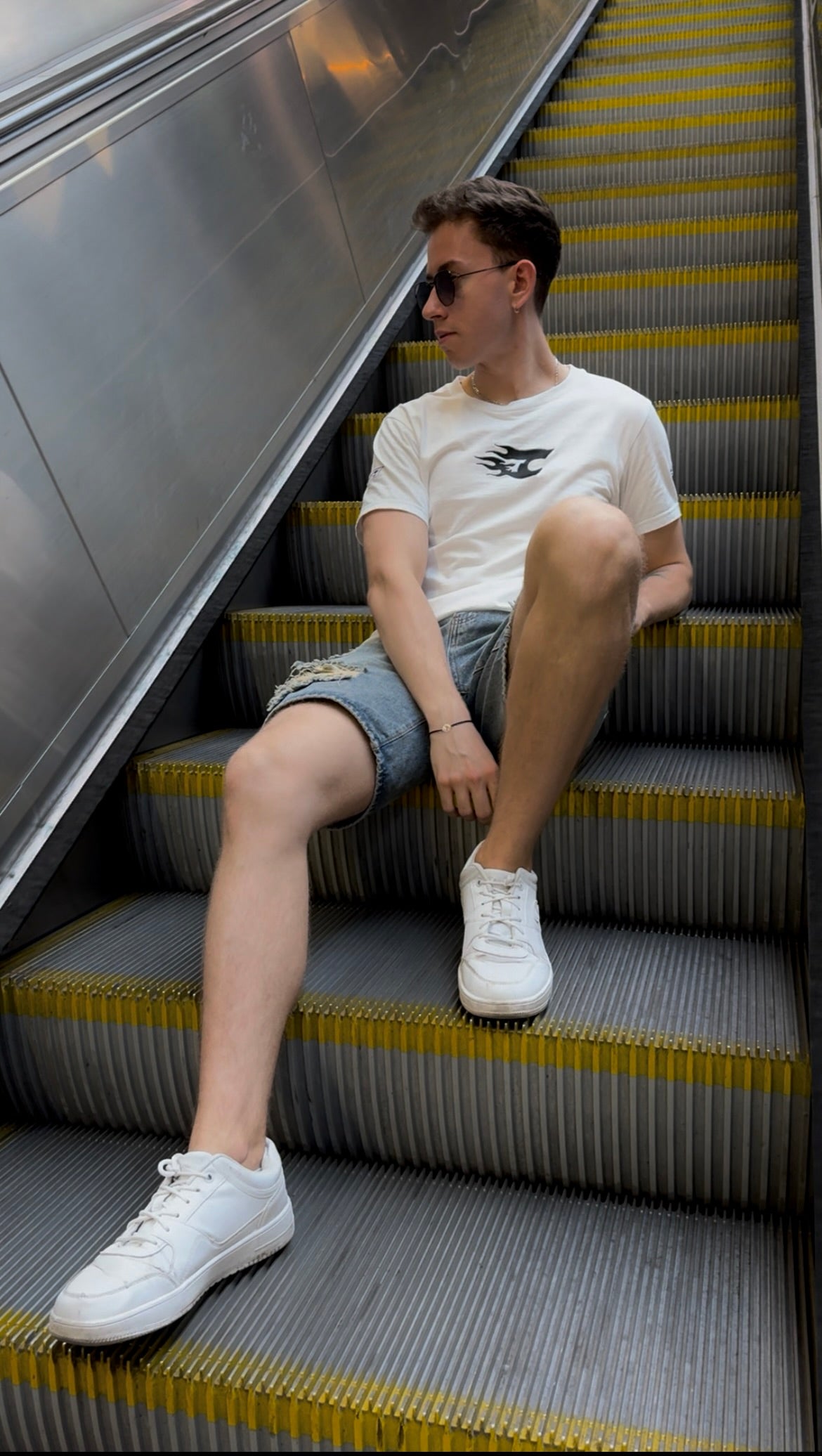 Person sitting on an escalator wearing a white t-shirt and shorts.