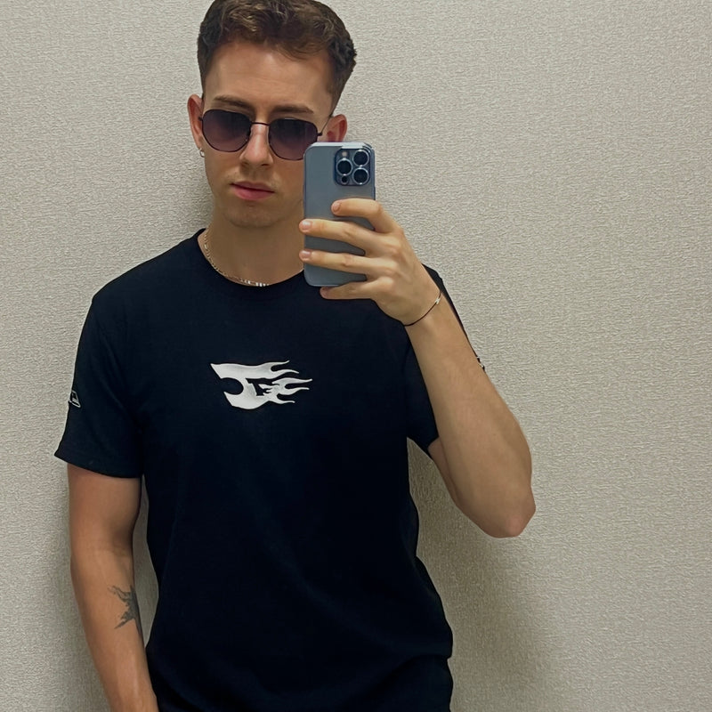 Person wearing a black t-shirt with a white logo, taking a mirror selfie.