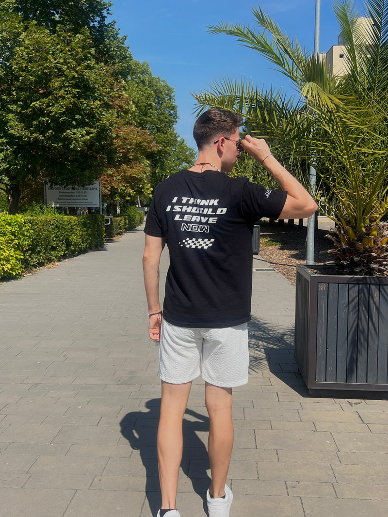 Person wearing a black t-shirt with text and white shorts walking outdoors on a sunny day.