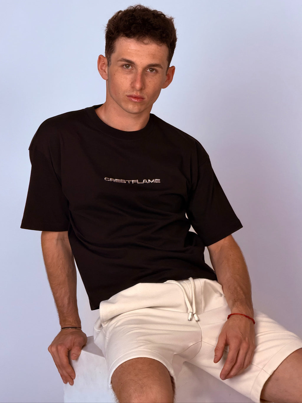 Man wearing a black t-shirt with text and white shorts sitting against a light blue background